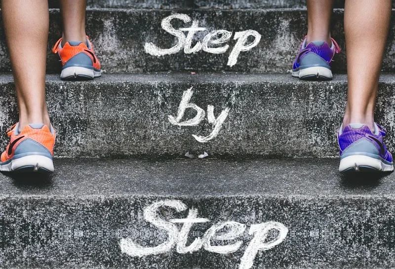 Schody z napisem step by step — metafora zmiany małymi krokami
